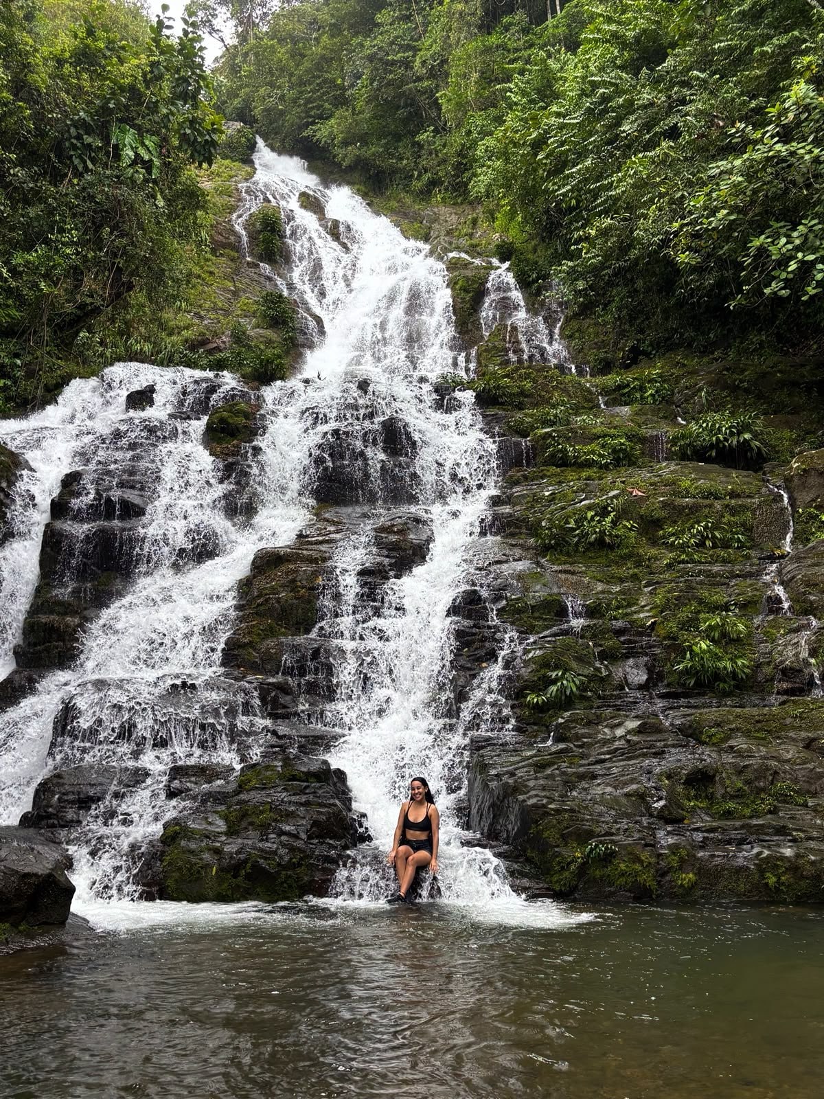 Yinelis sentada frente a una gran cascada rodeada de naturaleza